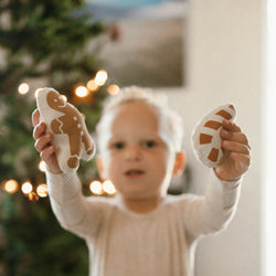 Child holding holiday-themed plush toys in front of a Christmas tree.