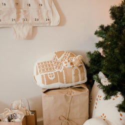 Festive holiday decor with gingerbread house cushion, wrapped gifts, and pine tree.