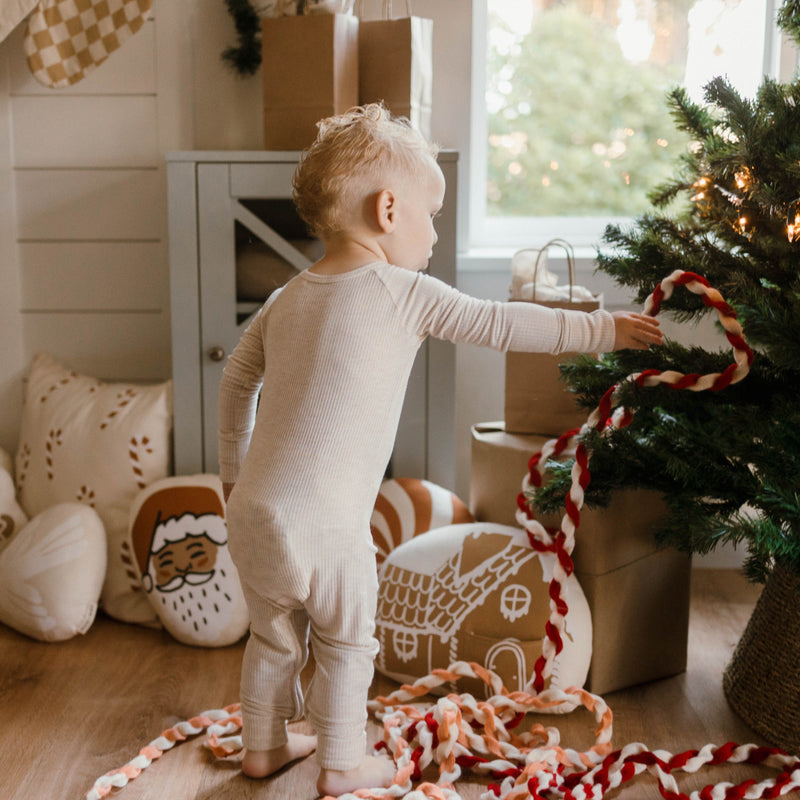 Toddler decorating Christmas tree with festive spool decorations in cozy living room.
