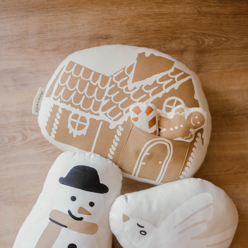 Soft gingerbread house and snowman-themed pillows on a wooden floor surface.