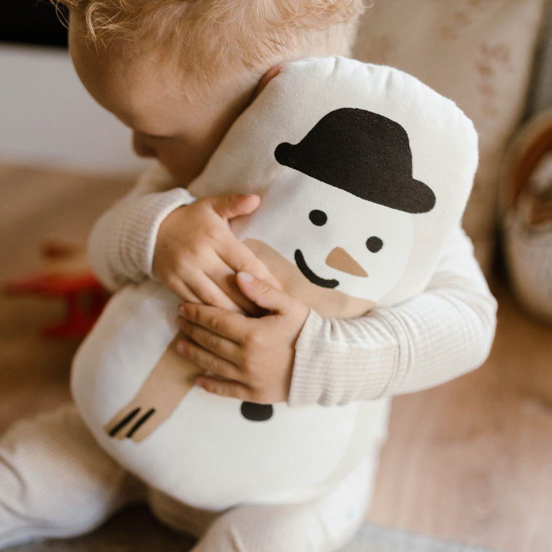 Toddler hugging a plush snowman toy while sitting on the floor.