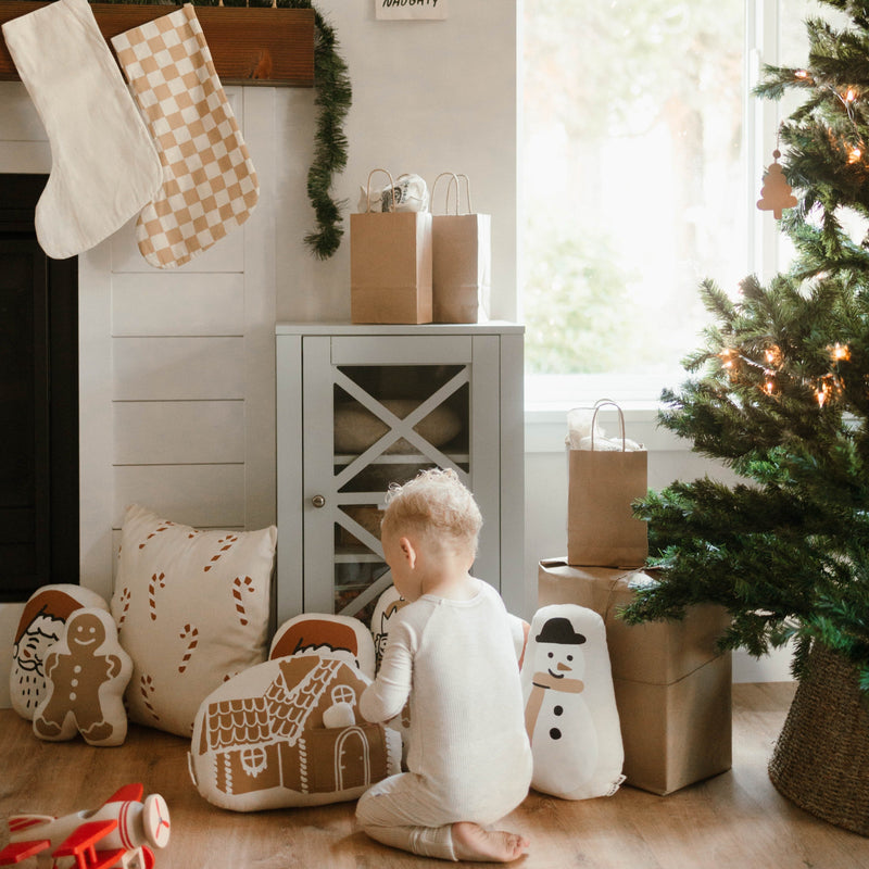 Toddler in pajamas enjoying Christmas morning with presents and festive decorations under a Christmas tree.