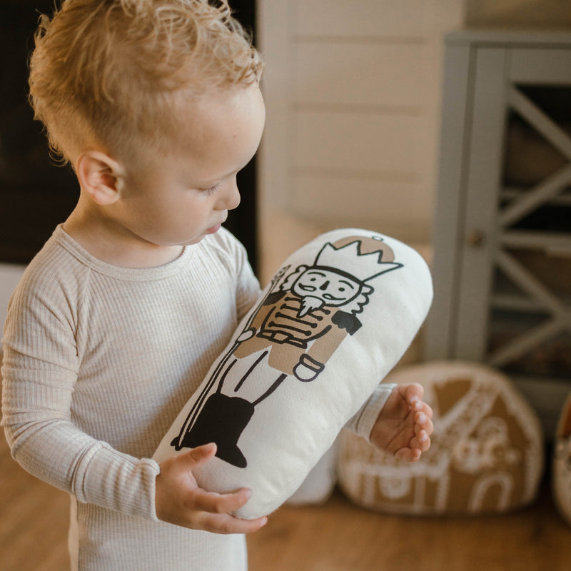 Toddler in striped pajamas holding a nutcracker-themed pillow in a cozy room setting.
