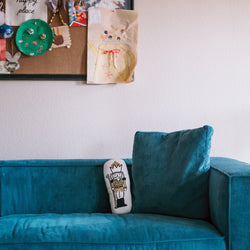 Children's art display on a wall above a teal couch with a decorative pillow.