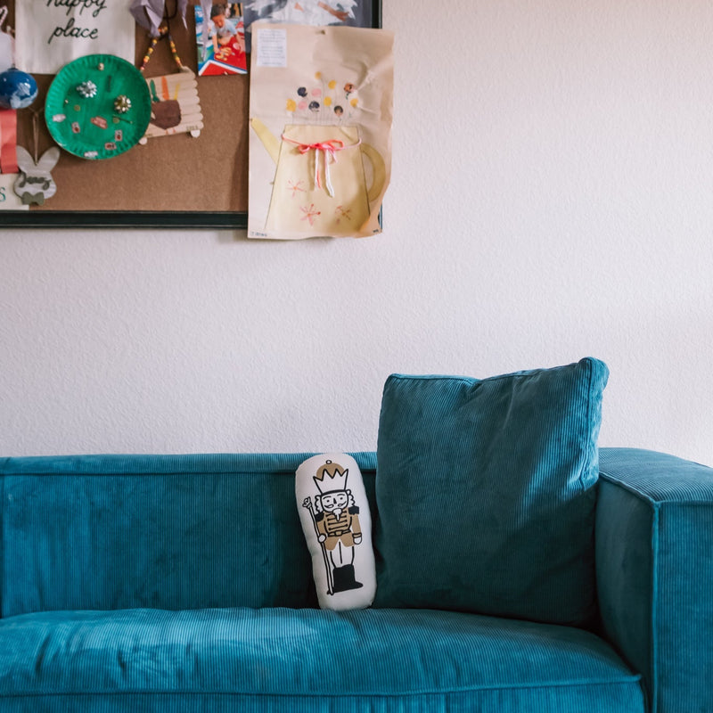 Children's art display on a wall above a teal couch with a decorative pillow.