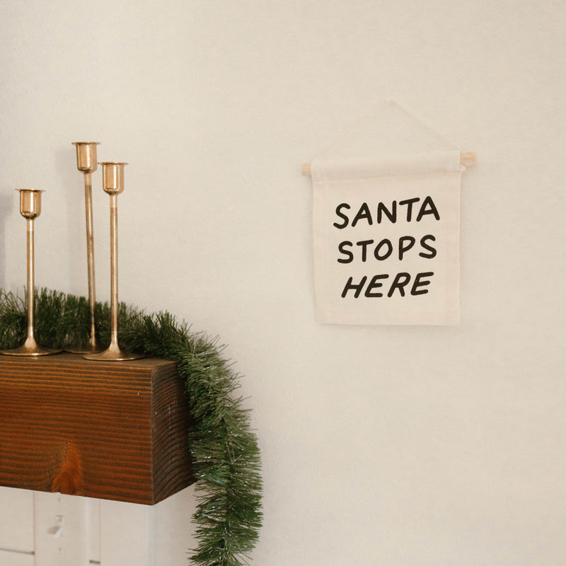 Christmas mantel decoration with "Santa Stops Here" sign and festive garland.