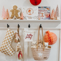 Christmas-themed mantle decoration with gingerbread cookie, pink Christmas trees, red ornaments, and a checkered stocking.