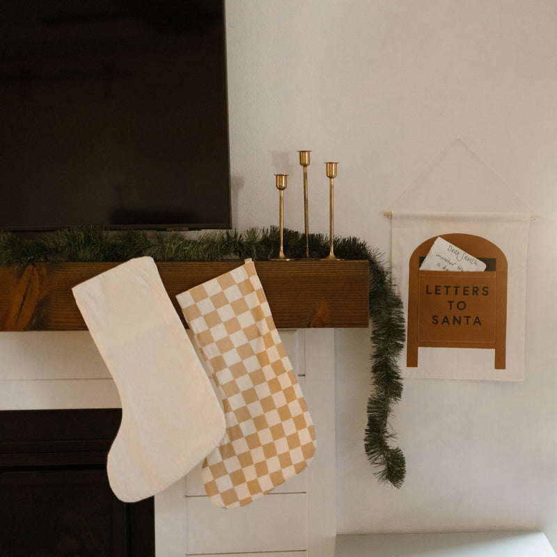 Christmas stockings hanging on a mantle with a "Letters to Santa" pouch, decorated with festive greenery.
