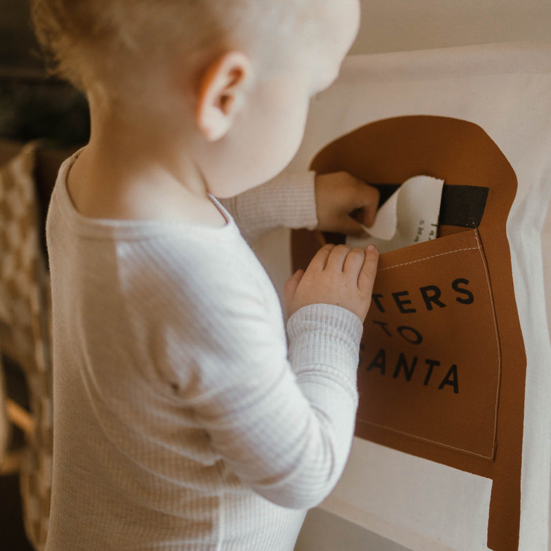Toddler inserting a letter into a "Letters to Santa" mailbox for Christmas.