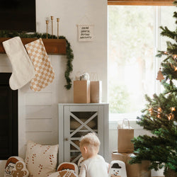Cozy Christmas living room with stockings, holiday decorations, and a child near the Christmas tree.