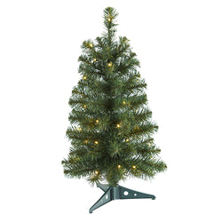 Small prelit artificial Christmas tree with warm white LED lights and realistic pine needles on a green plastic stand, tabletop holiday decoration