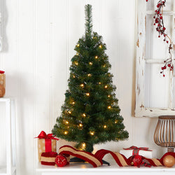Pre-lit artificial tabletop Christmas tree with warm white LED lights, red ribbon, ornaments and wrapped gifts against a rustic white shiplap backdrop
