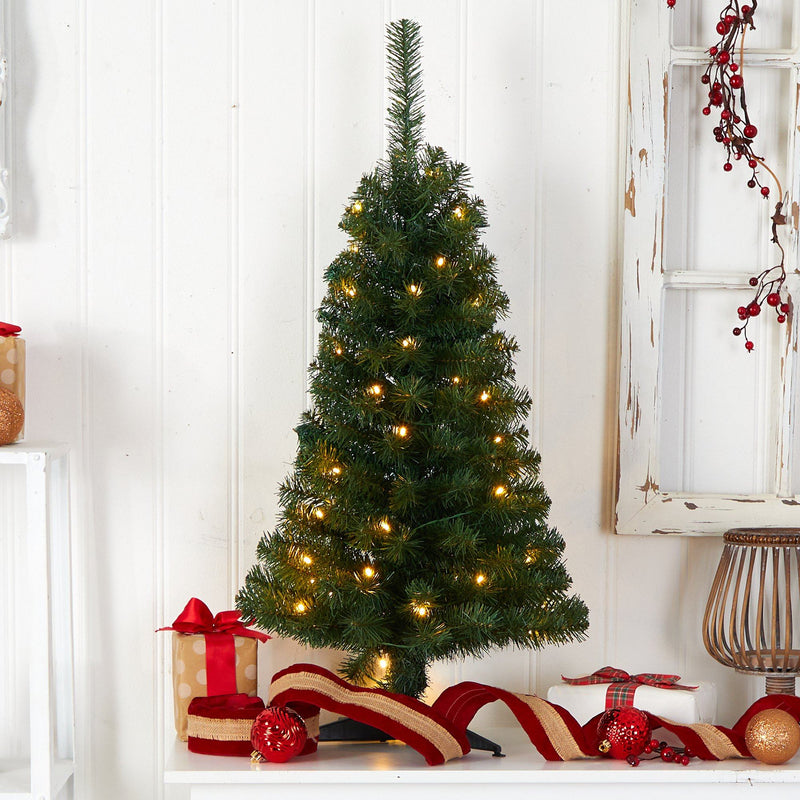 Pre-lit artificial tabletop Christmas tree with warm white LED lights, red ribbon, ornaments and wrapped gifts against a rustic white shiplap backdrop