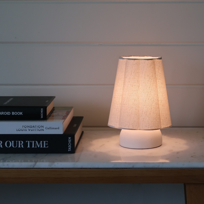 Warm-lit modern table lamp with beige linen shade on marble console table beside stacked coffee-table books