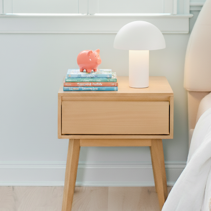 Wooden nightstand with books and a lamp next to a bed on a patterned rug.