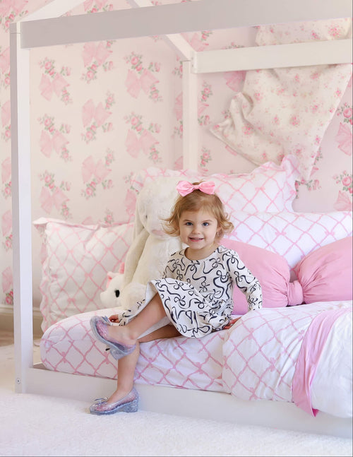 Toddler girl with pink bow sitting on a bed in a floral-themed nursery.