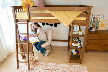 Child using a computer on a desk attached to a wooden bunk bed in a room with a dresser and decor.