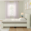 Cozy modern bedroom interior featuring an upholstered cream bed with mattress, pastel green vertical striped wallpaper, sheer white curtains, wooden nightstand with blue lamp and children's framed art