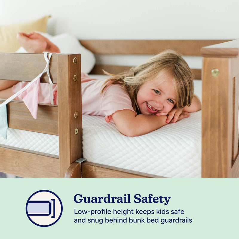 Smiling child lying on white mattress in wooden kids bunk bed with low-profile guardrail and pastel bunting