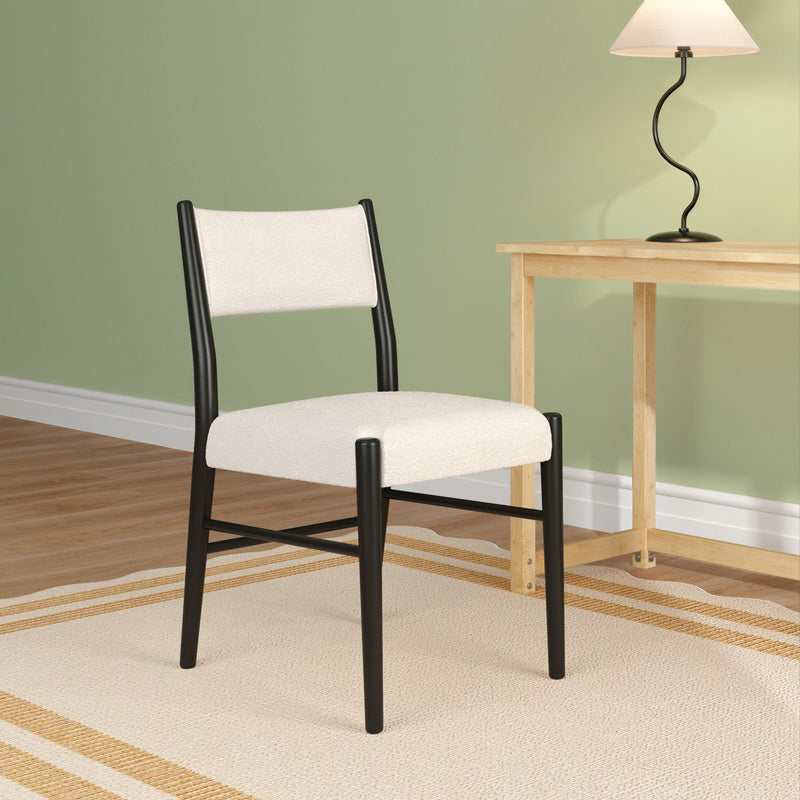 Minimalist modern dining chair with cream upholstery and black frame beside a natural wood side table and curved black table lamp against a sage green wall, hardwood floor and striped neutral rug