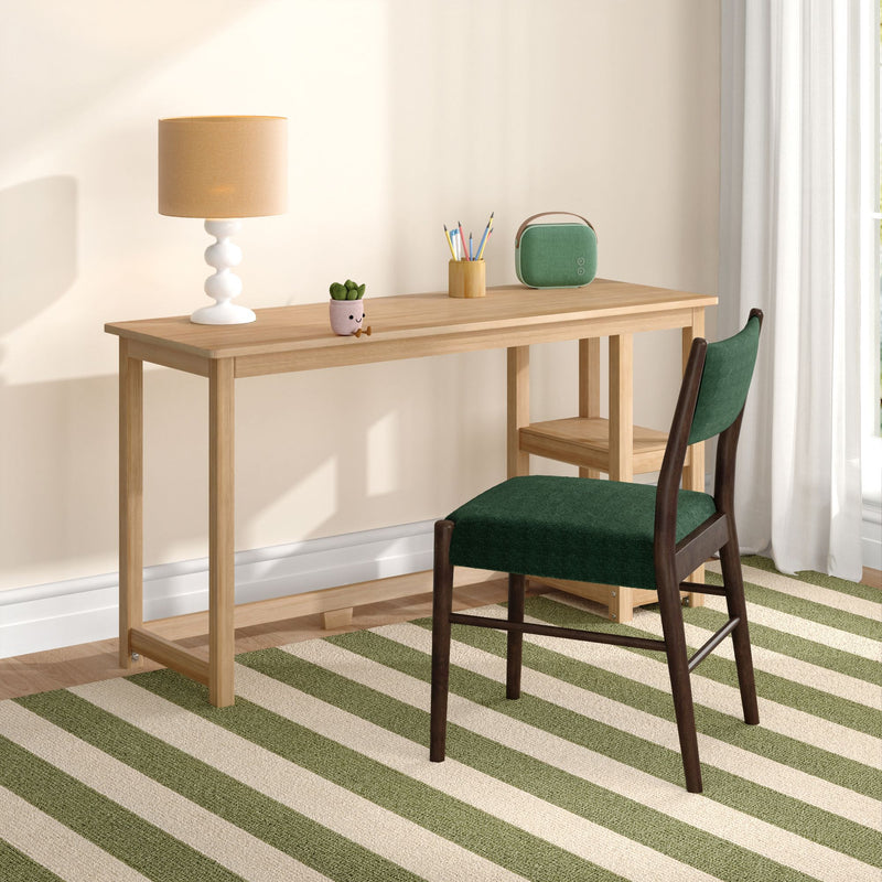 Minimalist home office desk setup: wooden table with beige lamp, potted succulent, pencil cup and green portable Bluetooth speaker beside a green upholstered chair on a striped rug.