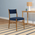 Blue upholstered mid-century modern dining chair beside a wooden side table with a beige table lamp and small succulent on a beige striped rug in a minimalist interior