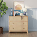 Light rattan three-drawer dresser in coastal nursery with whale sunset print, octopus plush toy, blue table lamp and potted fiddle-leaf fig