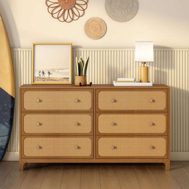 Six-drawer mid-century wood dresser with woven rattan cane drawer fronts, coastal boho bedroom styling with surfboard, table lamp, framed beach photo and potted plant