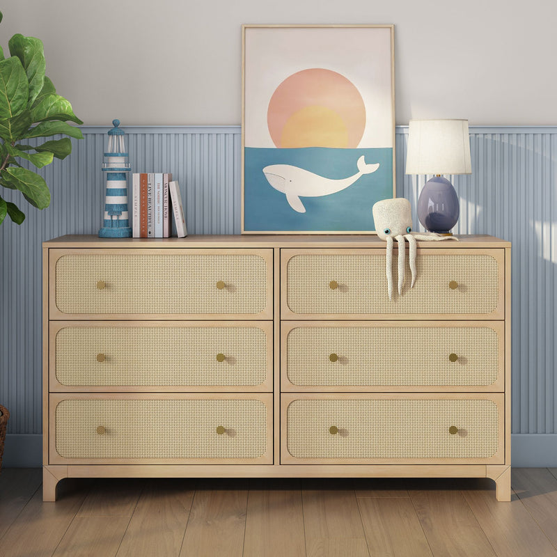 Natural wood rattan cane-front six-drawer dresser in coastal nursery, styled with whale wall art, blue lamp, plush octopus, lighthouse decor and books.