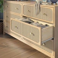 Woven cane-front natural wood dresser with brass knobs and open drawer containing folded clothes on hardwood floor — boho nursery or bedroom storage solution
