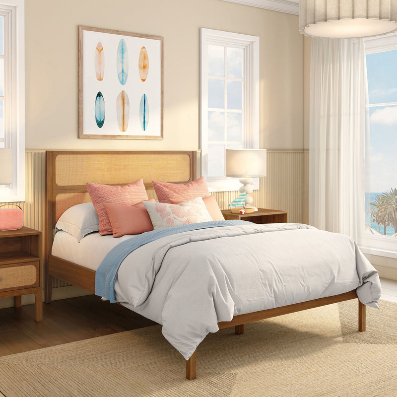 Modern coastal bedroom interior with light wood bed and woven rattan headboard, neutral bedding and blue throw, coral pillows, bedside lamps and large window overlooking ocean view