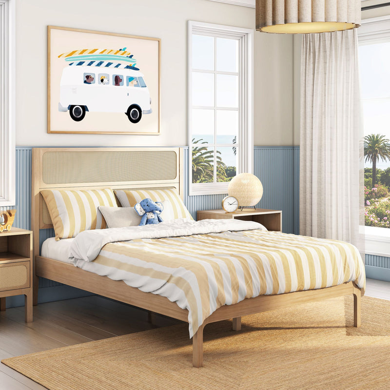 Beach-themed kids bedroom with wooden rattan bed frame, yellow-and-white striped bedding, blue stuffed toy, surf-van wall art, bedside lamp and clock, sheer curtains and palm-tree ocean view