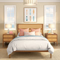 Coastal bedroom with rattan headboard, white bedding, coral and blue throw pillows, surfboard artwork, wood nightstands, table lamps and ocean-view windows