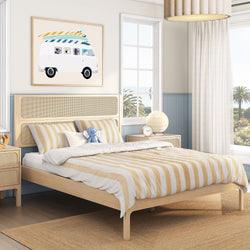 Coastal bedroom with light wood platform bed, beige-and-white striped bedding, rattan headboard and nightstand, blue wainscoting, ocean view and surf van wall art