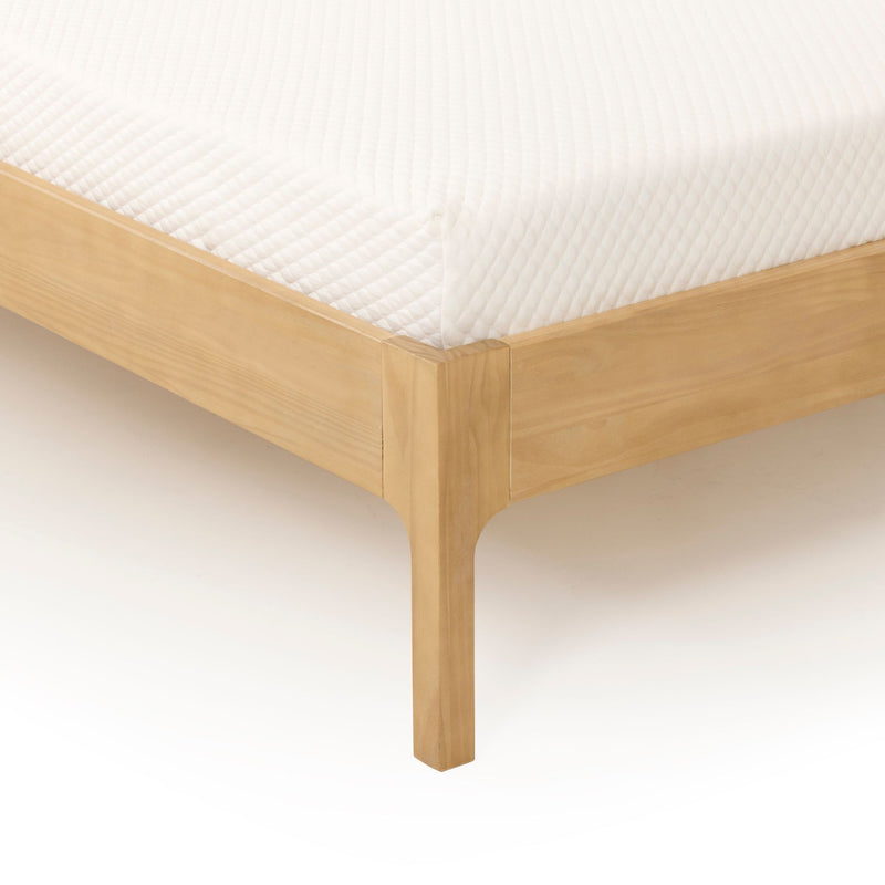 Close-up of a white quilted mattress cover on a light wood platform bed frame corner, showing mattress texture and bed frame detail