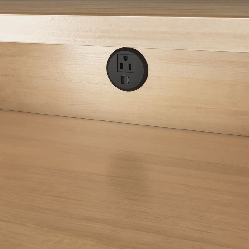 Round black recessed desk power outlet with AC socket and USB-A and USB-C ports mounted in light wood