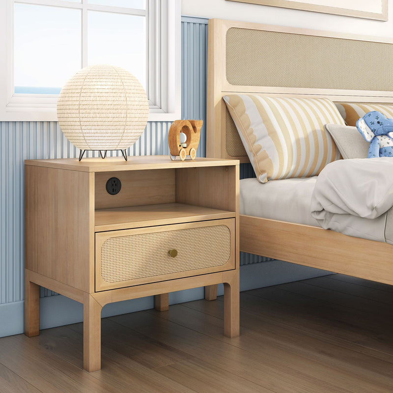 Light wood nightstand with woven cane drawer and paper lantern lamp beside striped pillow on coastal-style bedroom bed