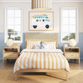 Beach-themed children's bedroom with beige and white striped bedding on a light wood bedframe, surfboard-van wall art, ocean view through two windows, matching nightstands with round lamps and a plush elephant toy