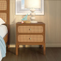 Mid-century wooden nightstand with natural cane rattan drawer fronts, white ceramic lamp and small nautical sailboat on top in a coastal bedroom interior