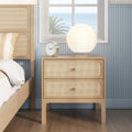 Light wood rattan bedside table with round paper lamp and gold alarm clock in a coastal bedroom with ocean view through window