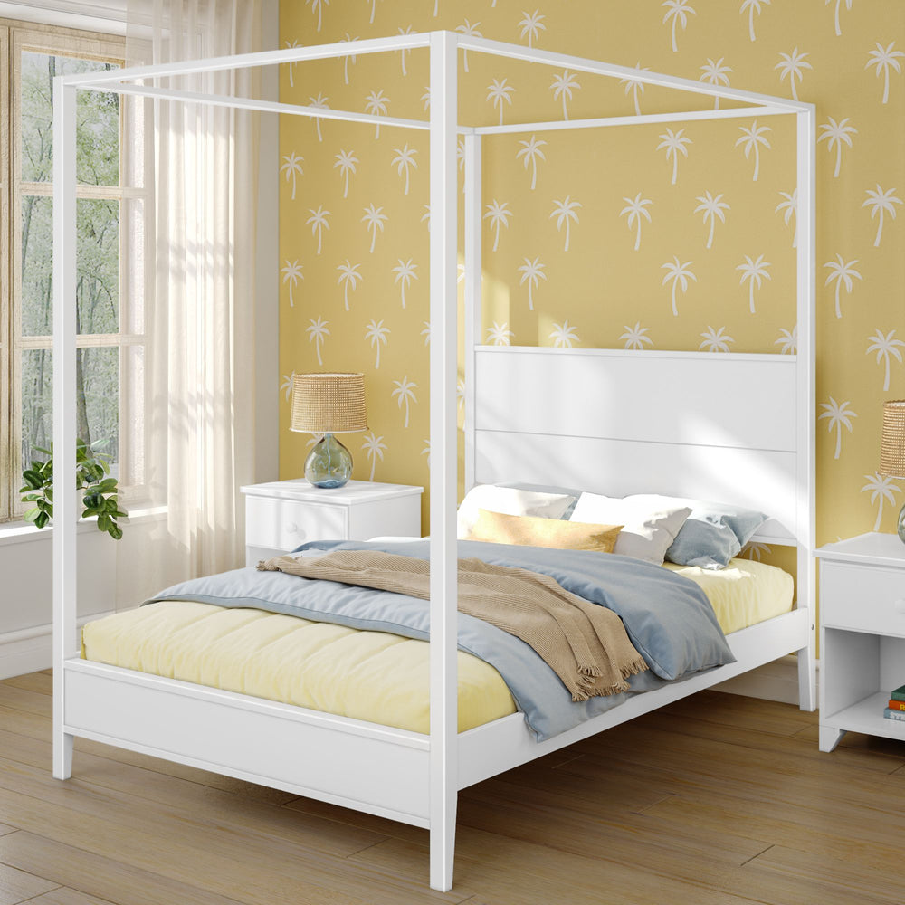 White four-poster bed in a sunny bedroom with tropical palm tree wallpaper, featuring modern nightstand and cozy bedding.