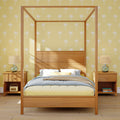 Wooden four-poster canopy bed with pastel bedding in a coastal bedroom featuring yellow palm-print wallpaper, matching nightstands and glass lamps