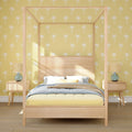 Modern coastal bedroom with light wood canopy bed, yellow palm-print wallpaper, rattan bedside lamps and pastel blue and yellow bedding