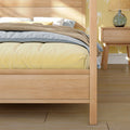 Cozy modern bedroom with light wood bed frame, yellow duvet, blue sheets, beige textured throw, white pillows and bedside table with glass lamp against palm-print wallpaper