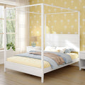 Sunlit bedroom with white canopy bed, yellow palm wallpaper, cozy blue-beige bedding, bedside lamp and plant