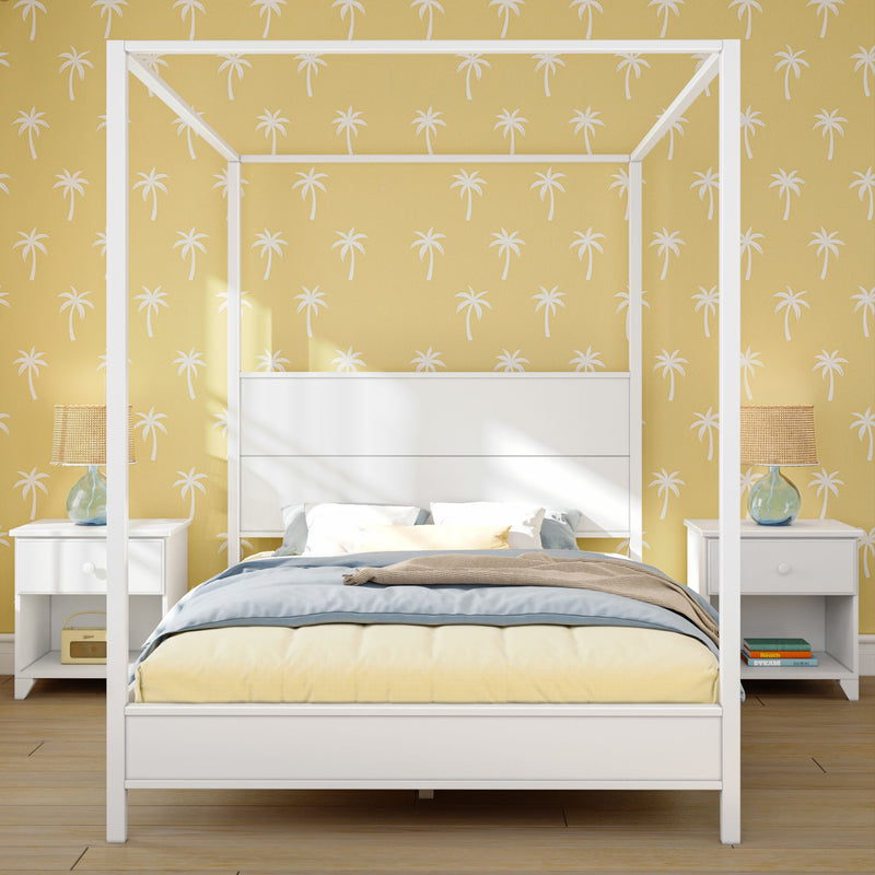 White canopy bed with yellow and blue bedding, palm tree patterned wallpaper, and nightstands with lamps in a modern bedroom.