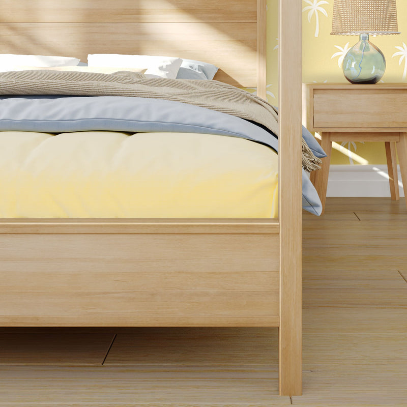 Light oak canopy platform bed with yellow duvet, blue sheets and beige throw in a coastal-style minimalist bedroom with palm-print wallpaper and wooden nightstand lamp.