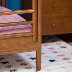 Mid-century modern wooden toddler bed frame with pink mattress on a multicolor polka-dot shag rug in a children's bedroom