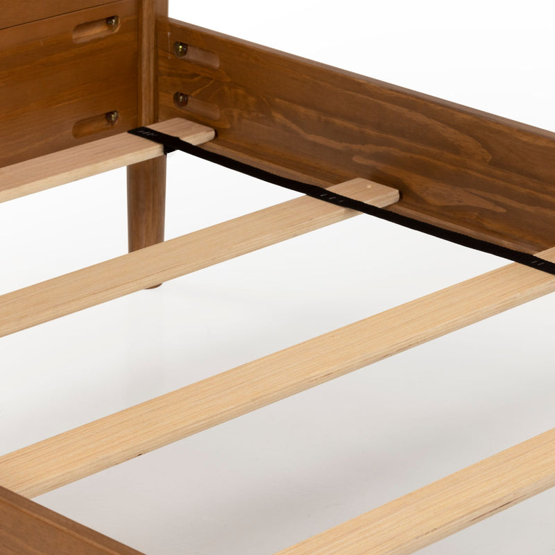Close-up of a wooden bed frame platform showing light wood slats, dark stained side rails and a black center support strap for mattress support
