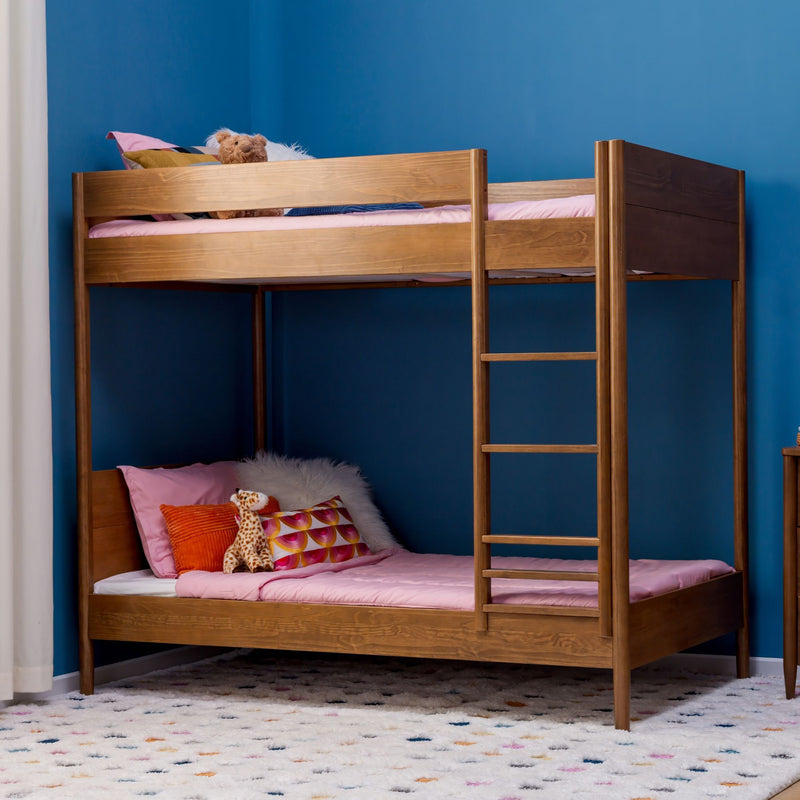 Wooden bunk bed in kids' bedroom with blue accent wall, pink bedding, ladder and plush toys